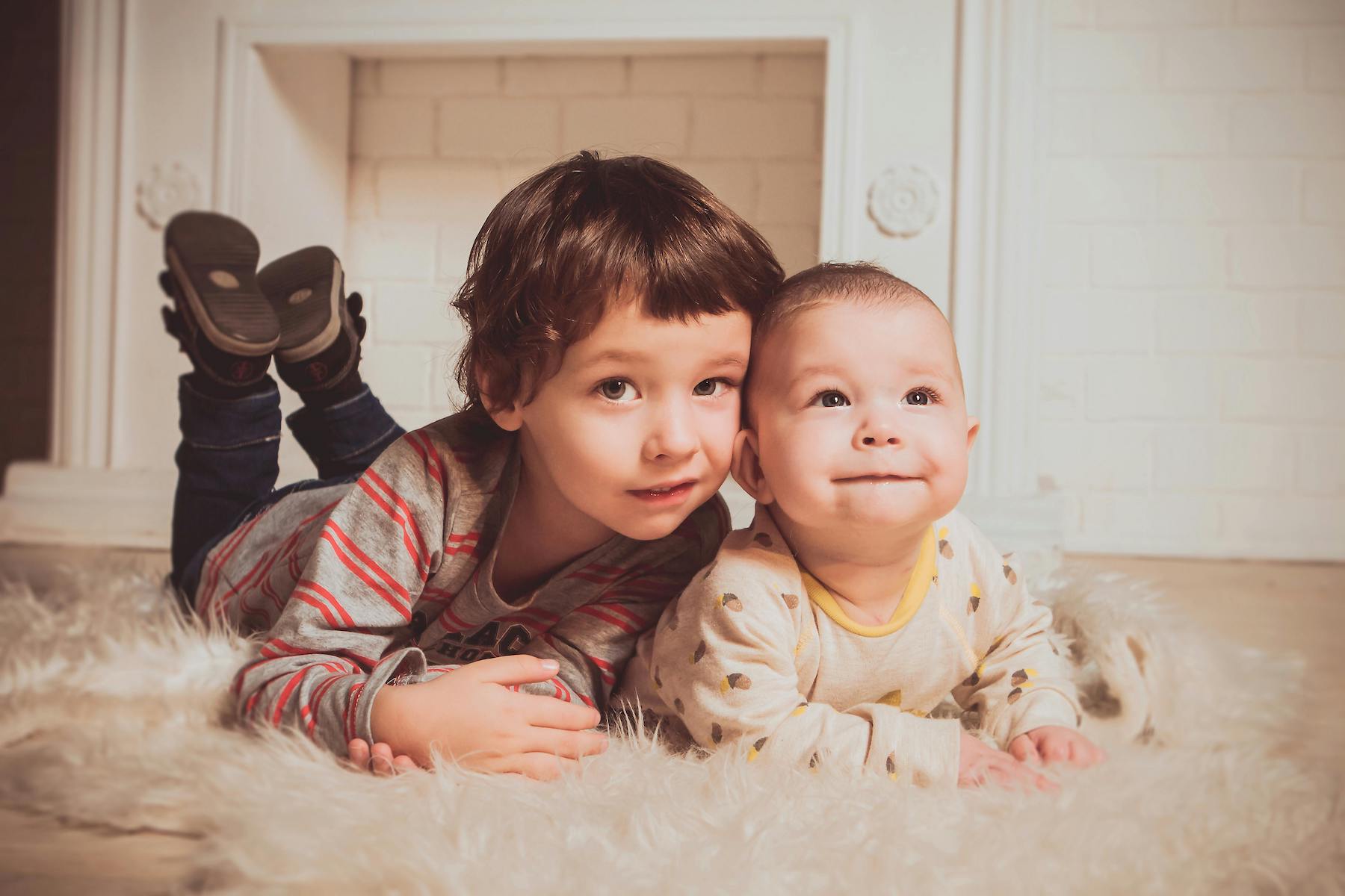 two young boys a toddler and baby laying on a rug together